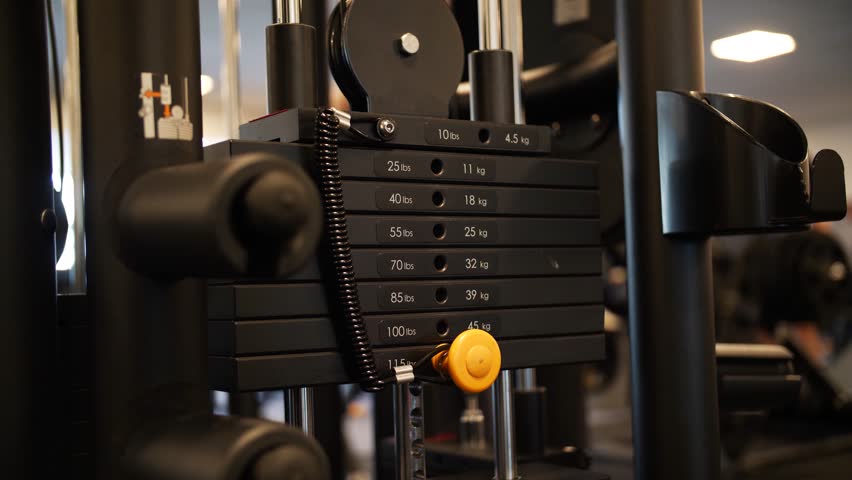 Slow motion close-up of a gym machine in action, emphasizing the movement of weights up and down