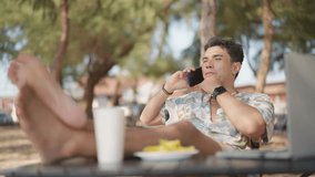 Asian man working business on laptop computer and speaking on mobile phone during travel the beach on summer vacation. Workation, work from anywhere with wireless technology and digital gadget device. - Powered by Shutterstock - Get 15% off with code: PIKWIZARD15
