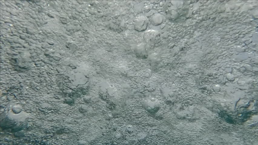 Close-up slow motion of rain water drops falling on surface of water in heavy tropical downpour, underwater shot
