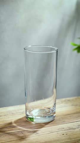 fresh clean water pouring into a glass on sunny wooden kitchen tabletop and gray wall background, slow motion