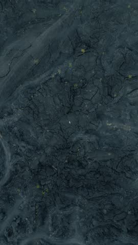 Aerial view of a volcanic landscape showcasing dark, cracked lava with sparse vegetation, revealing the stark contrast of nature's raw power.
