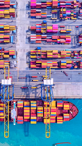 Time lapse of cranes loading and unloading containers from a cargo ship at a deep-sea port. Vertical clip.