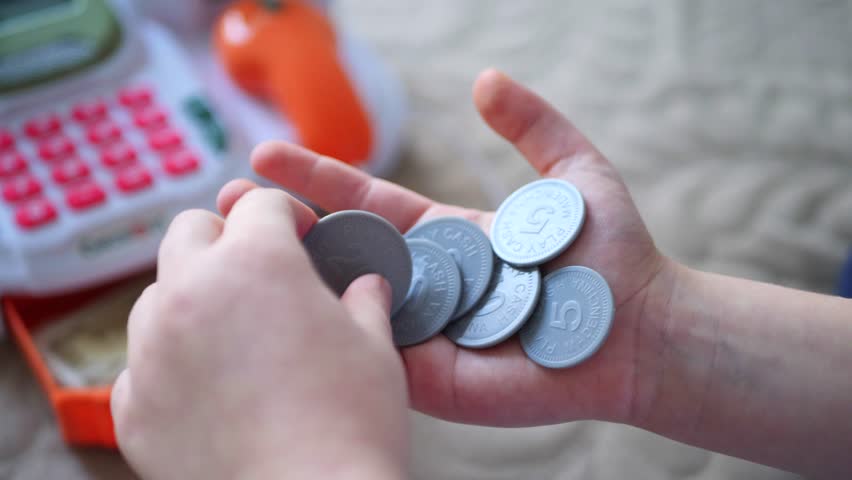 A child's hand, full of play money, ready to make a purchase. Playful coins, nestled in a hand, hinting at a pretend market. The satisfying clink of play money, a child's delight. A miniature market