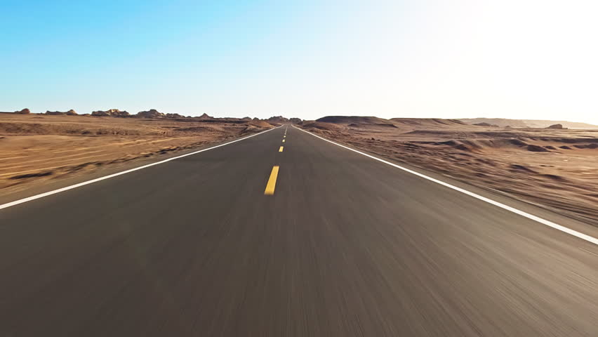 Wide asphalt road stretching into the horizon through a barren desert landscape 