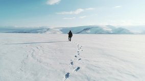 A photographer explores a vast snow-covered landscape, leaving a trail of footprints behind. The sun casts a long shadow on the frozen ground, highlighting the untouched winter terrain. - Powered by Shutterstock - Get 15% off with code: PIKWIZARD15