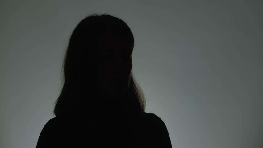 Anonymous interview with a woman who suffered from violence. Female silhouette. Hidden person speaking in a dark studio.