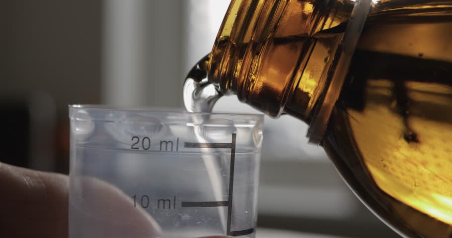 A man pours medicine into a measuring cup. Close-up.