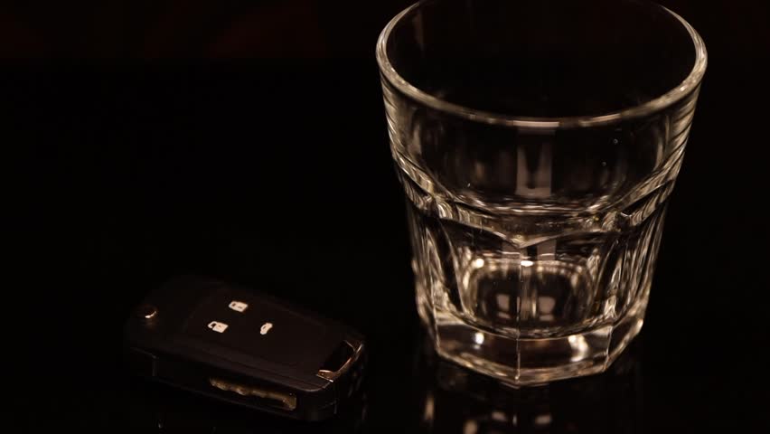 Pouring alcohol into a glass with a car key sitting next to it.