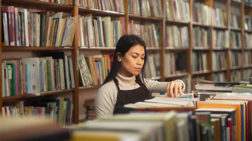 Concentrated worker organizing books in a secondhand bookstore. Focused employee arranging the shelves in a quiet and tidy shop environment.
