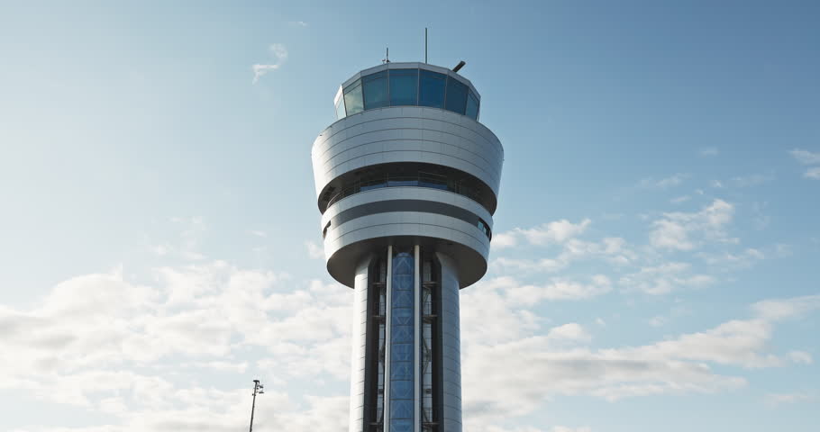 Modern airport control navigation tower for airplanes against bright blue sky with clouds on a sunny day 