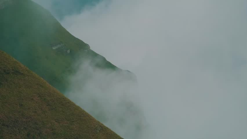 Misty mountain ridge unveiling through rolling clouds and vibrant green hills