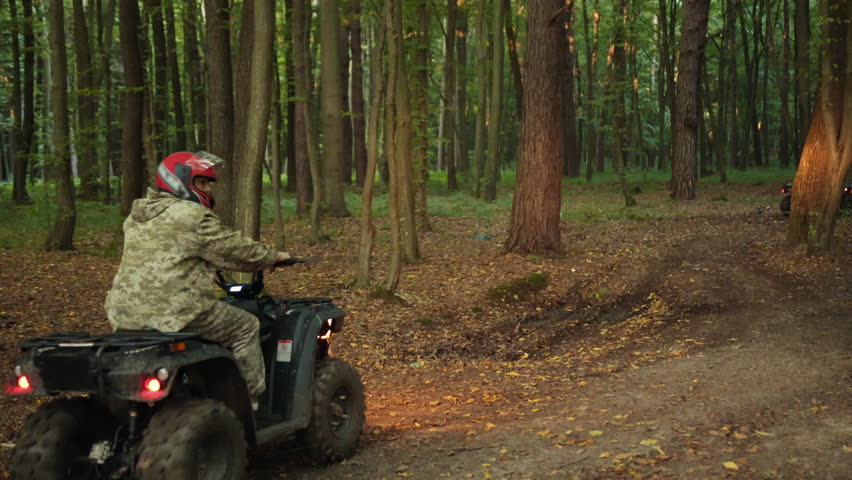 Helmeted group, Navigating woods, ATV trail. Wearing helmets and camouflage, group people navigate ATVs through forest trail with their headlights on.