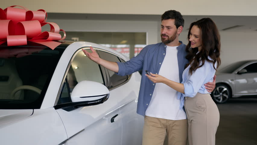 Caucasian happy family choosing vehicle talking woman wife girlfriend girl female holding key from new car hug man male guy boyfriend husband buying electric auto couple automobile purchase dealership