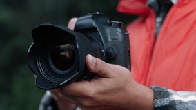 Professional photographer wearing bright orange jacket adjusting camera lens while standing outdoors, capturing detailed natural landscape with precision - Powered by Shutterstock - Get 15% off with code: PIKWIZARD15