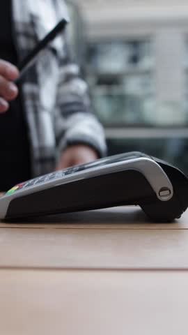 Customer making contactless payment, using smartphone near pos terminal, completing wireless financial transaction with modern digital technology