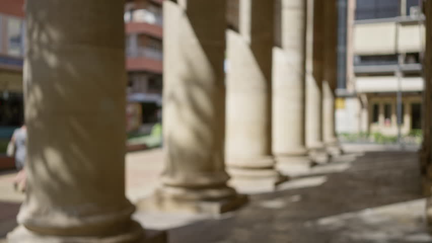 Blurred view of stone pillars in an outdoor urban area with sunlight casting shadows on the ground
