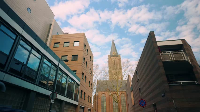 Historic church stands between modern buildings in Utrecht, showcasing blend of old and new architecture. Brick facade contrasts with glass and steel structures under a blue sky. Utrecht | Nederland