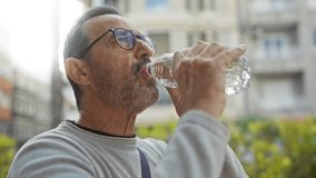 Middle aged hispanic man drinking water from plastic bottle outdoors in urban park setting wearing casual shirt and glasses with focus on hands and bottle. - Powered by Shutterstock - Get 15% off with code: PIKWIZARD15