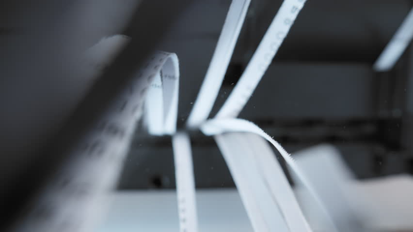 A close up view of a paper shredder cutting a sheet of office paper, document into thin strips.