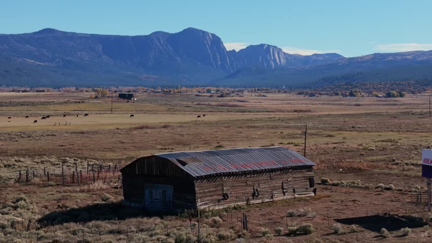 Expansive New Mexico landscape with mountains, a barn, and grazing cattle in the distance