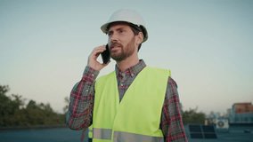 Project manager on call discusses solar panel installation updates, sustainable energy goals. Caucasian young man in helmet talking on mobile phone. Male worker speaking on telephone outdoor. - Powered by Shutterstock - Get 15% off with code: PIKWIZARD15