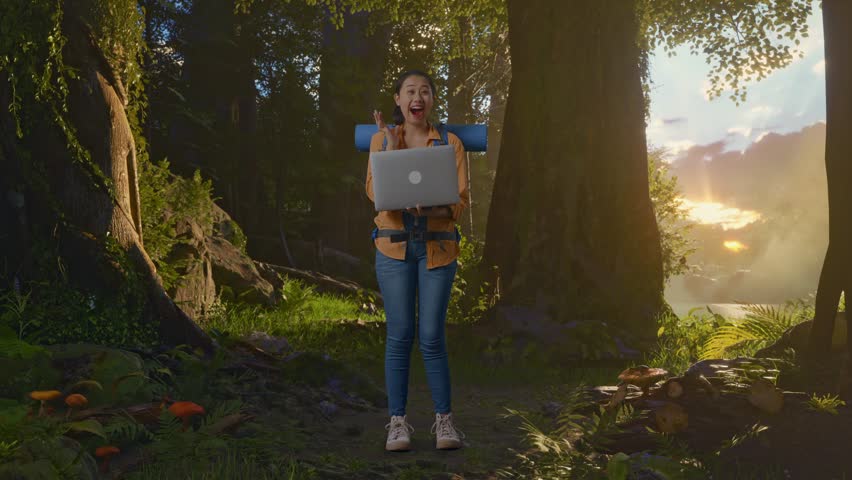 Full Body Of Asian Female Hiker With Mountaineering Backpack Looking At A Laptop And Saying Wow While Exploring Forest Nature