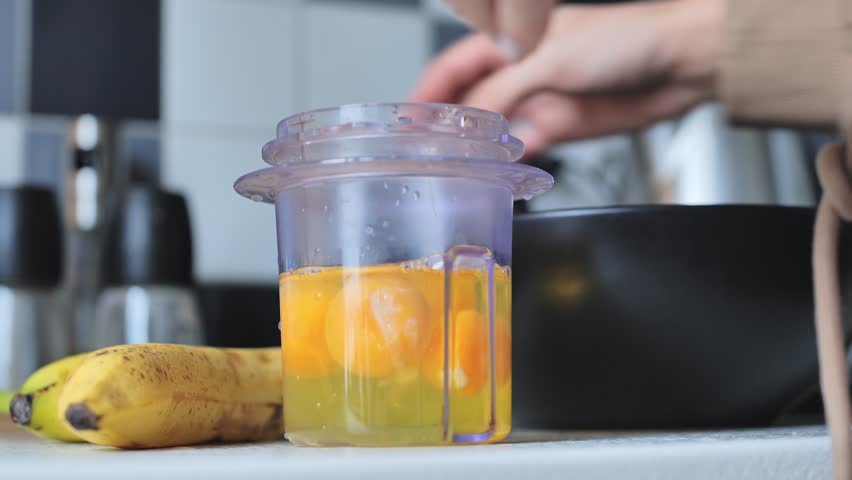 Fresh eggs in a blender cup with bananas being added for a nutritious mix - 4K