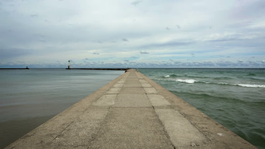 Concrete pier with calm water on one side and waves breaking on the other.