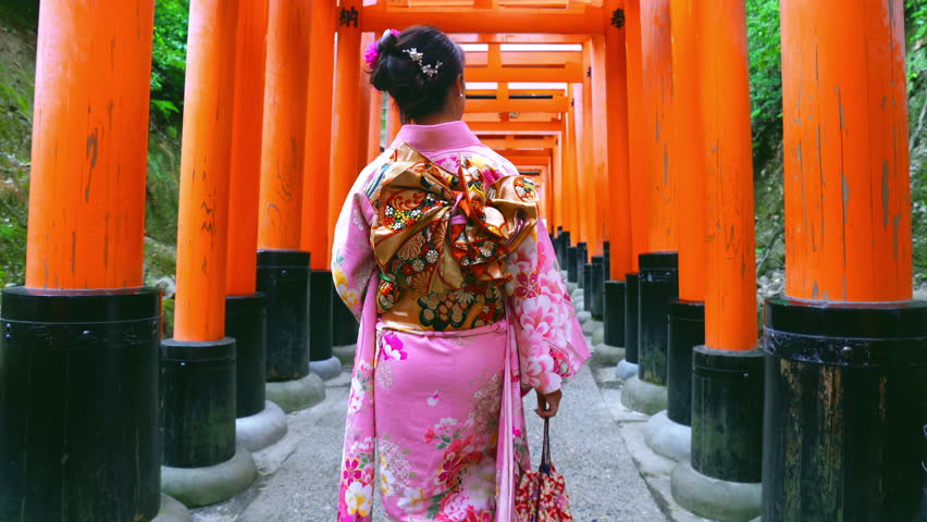 Asian women in traditional japanese kimonos visiting at Fushimi Inari Shrine in Kyoto, Japan. Translation: "to offer or to give".