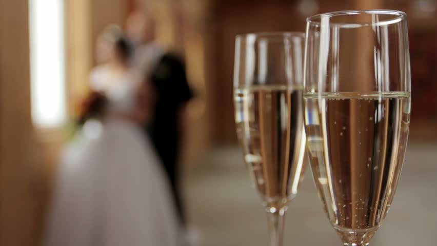 Two Champagne flutes sharp in foreground with bride and groom in soft focus in
