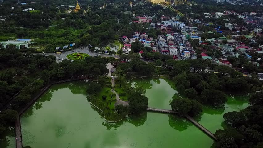 A breathtaking rising aerial over Kandawgyi Lake, Yangon, Myanmar, revealing the iconic Shwedagon Pagoda and the U Htaung Bo roundabout. Perfect for showcasing the city