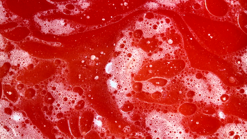Detail of white foam bubbles revolving in a container full of red fluid,