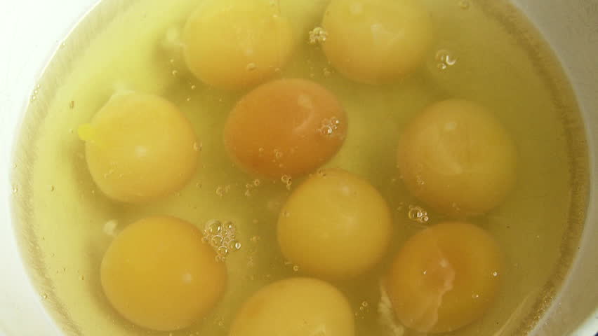 Fresh egg drops into a bowl with other yokes and whites. Slow motion, recorded