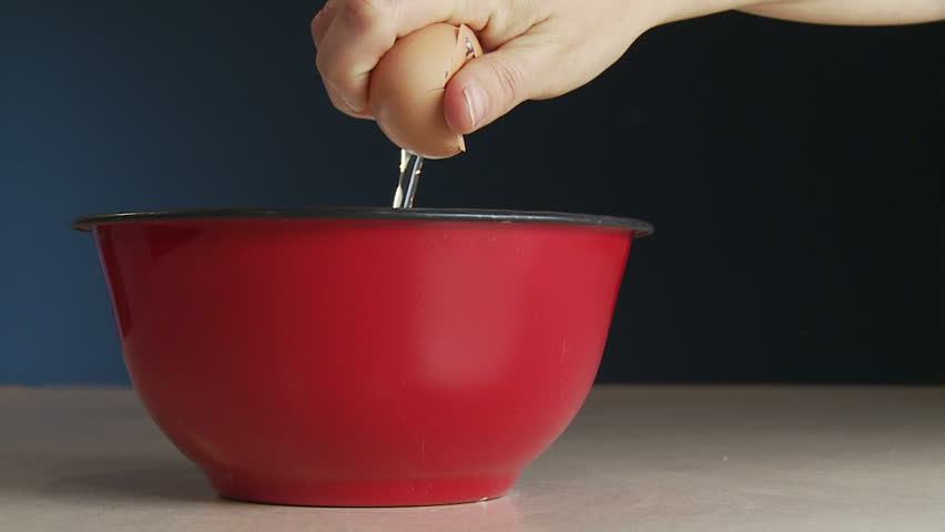 Hand breaks a fresh egg and drops it into a red bowl. Slow motion, recorded at