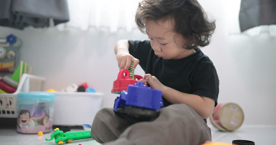 Asian toddler plays with a STEM toy engineering set at home, developing fine motor skills, problem-solving, and creativity. Natural light highlights early childhood learning and curiosity.