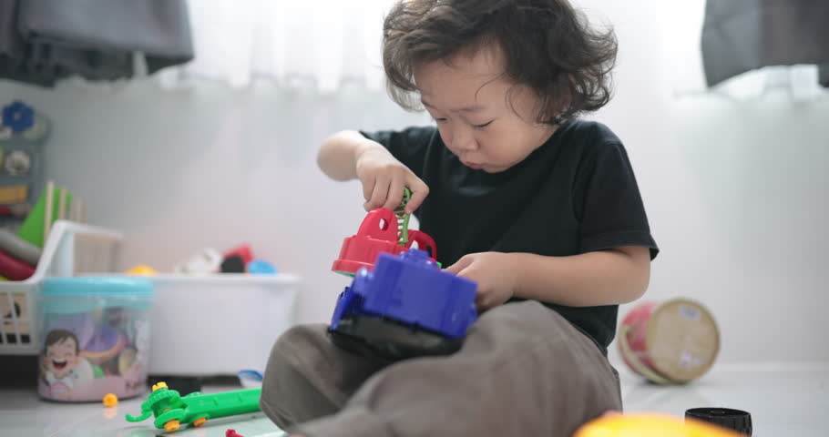 Asian toddler plays with a STEM toy engineering set at home, developing fine motor skills, problem-solving, and creativity. Natural light highlights early childhood learning and curiosity.