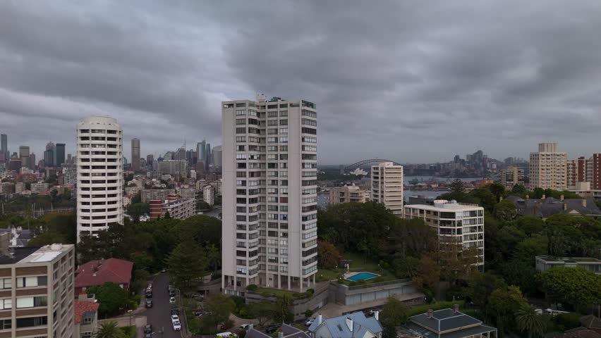 Sydney city skyline aerial view with high rise apartment buildings and rooftops revealing Harbour Bridge and Opera House in distance in morning light from Double Bay and Darling Point. Track R to L