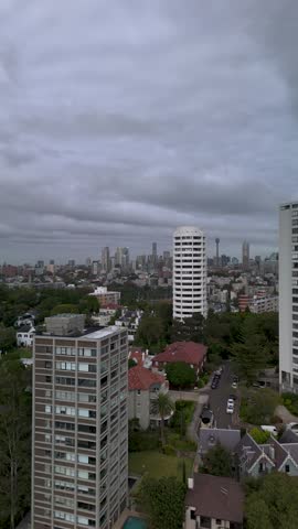 Sydney city skyline vertical aerial view with high rise apartment buildings and rooftops revealing Sydney Harbour Bridge and Opera House in distance in morning light from Double Bay and Darling Point.