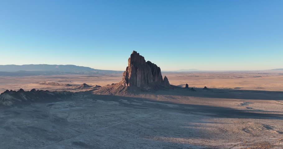 An unworldly high and far, wide-angle aerial shot of the sacred “Ship Rock”, a massive, monolithic monadnock, towering above the high desert plain of the Navajo Nation, in New Mexico, United States.