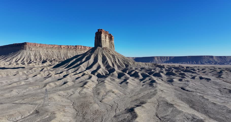 An unworldly, wide-angle drone shot, approaching an isolated, monolithic rock pillar known as Chimney Rock, or Jackson Butte, located in the Mesa Verde Region, in the southwestern corner of Colorado