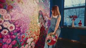 Talented woman artist carefully adding details to a large floral artwork, sitting on a stool and holding a palette with vibrant colors in her art studio - Powered by Shutterstock - Get 15% off with code: PIKWIZARD15