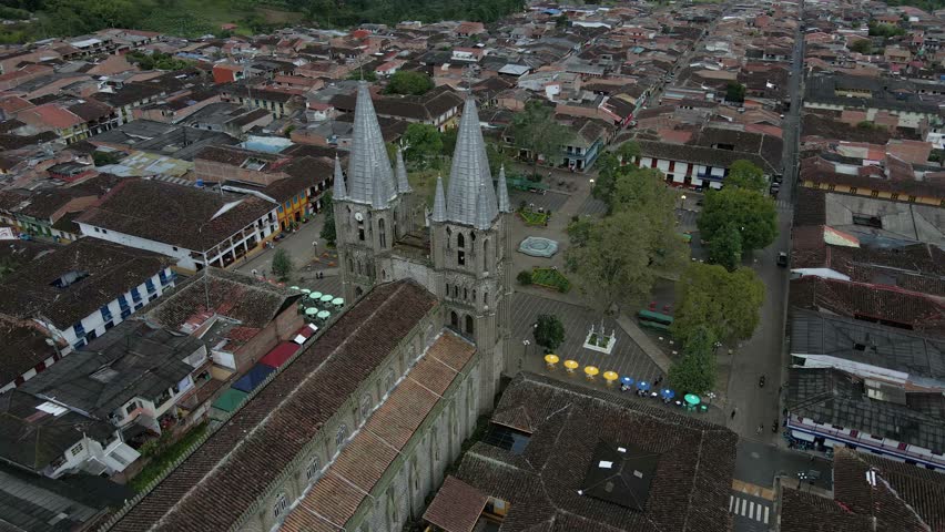 Aerial orbit of Basilica of the Immaculate Conception in Jardin, Colombia, colorful town streets surrounded by lush green hills
