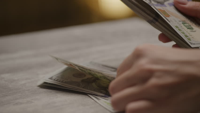 Hands counting stack of hundred-dollar bills on table