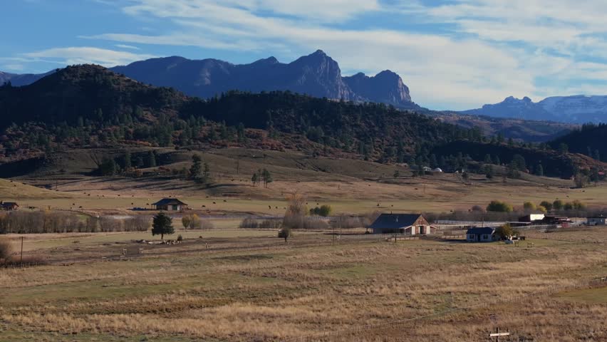 Serene ranch view in Colorado, vast open fields surrounded by rolling hills and distant mountains