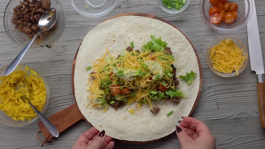 Hand wrapping tortilla with contents in envelope. Making burrito. Top shot. Slow motion. High quality 4k footage