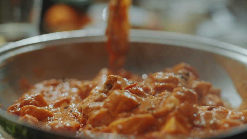 Extreme close-up shot of hand stirring creamy paneer butter masala in pan, mixing ingredients during cooking process of flavorful Indian dish