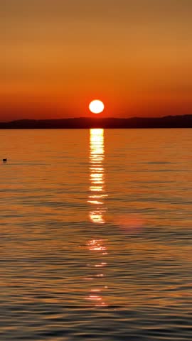 golden bright orange sunset at Italian Garda lake with the duck in summer with sun disk going down under the water	
