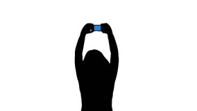 Silhoutted woman taking pictures or video with a cellphone. Black and white silhouette (with screen colored blue) isolated on white background.