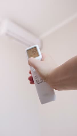 Woman turning on air conditioner to create a cozy atmosphere and warm up the room on an autumn evening.