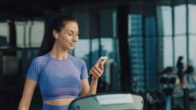 Young woman in sportswear walks on treadmill checking smartphone in gym. Lady engaged with social media balances fitness and technology in active lifestyle. Blogger creates content - Powered by Shutterstock - Get 15% off with code: PIKWIZARD15